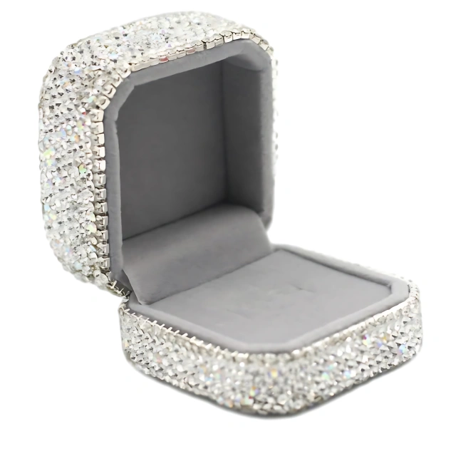 An open jewelry box encrusted with shimmering rhinestones, featuring a plush gray interior lining.