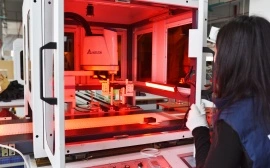 Female technician using automated laser processing machine in factory workshop with red laser beam visible inside the device