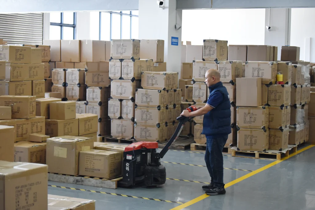 jewelry box factory worker using pallet jack to transport packaged luxury boxes in warehouse storage area