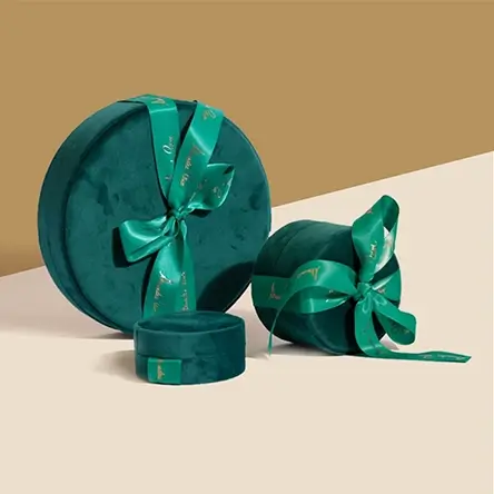 Round dark green velvet jewelry boxes with satin ribbon bows, in small, medium, and large sizes for gifting.